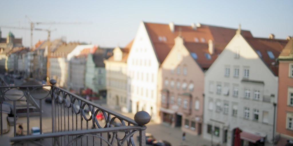 Blick über den Dächern Augsburgs von LE MOUV Studio aus auf die bunte Häuserfront der Maximilianstraße, mit einem verschwommenen Blick in Richtung Moritzplatz.