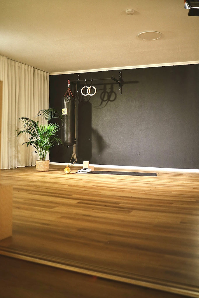 Blick durch den großen Spiegel in den Yogaraum des LE MOUV Studios: Die Matte der Lehrerin, umgeben von einer grünen Pflanze und Kerzenlicht.