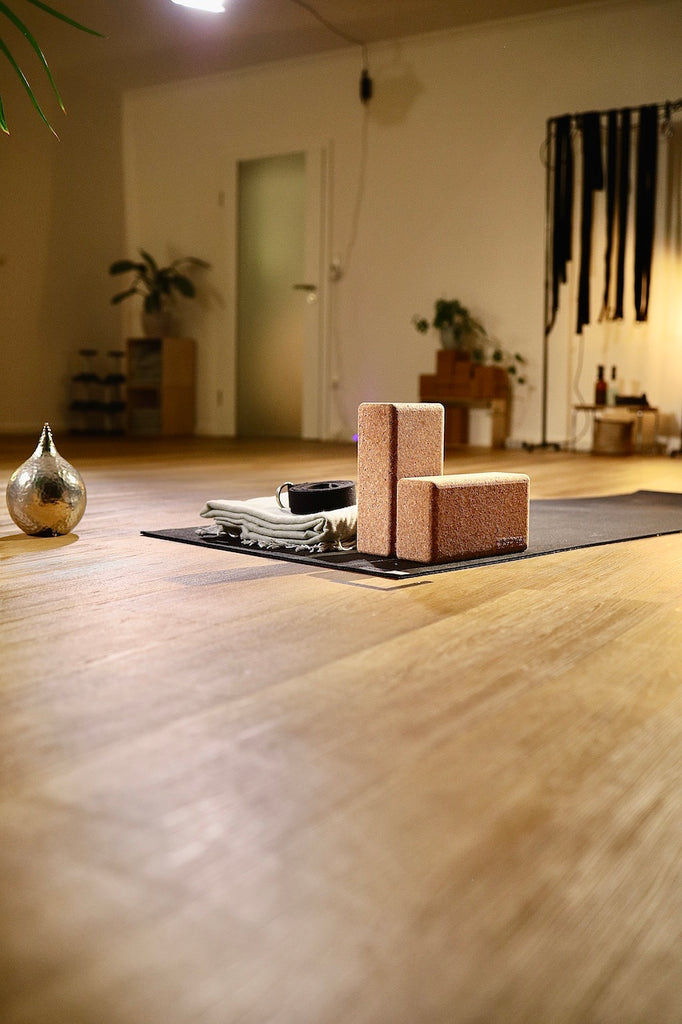 Yogaequipment, bestehend aus Yogablöcken, einem Yogagurt und einer Decke, liegt auf einer Yogamatte im gemütlichen LE MOUV Studio, bereit für eine professionelle und stimmungsvolle Yogapraxis.