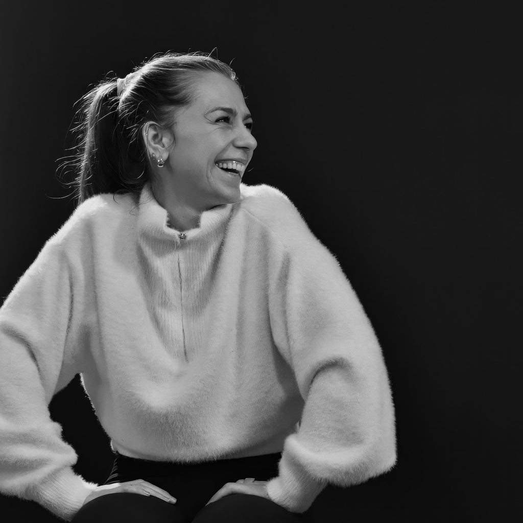 Irene Endres, Yogalehrerin im LE MOUV Studio, sitzt im Fersensitz mit einem strahlenden Lächeln und verkörpert mitreißende Energie und Kompetenz.